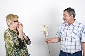 picture of blue sky  - Middle adult husband offering flowers to her wife and she is excited and pleasantly surprised - JPG 