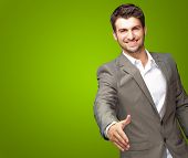 image of handshake  - Portrait Of Young Businessman In A Suit Holds Out His Hand For A Handshake On Green Background - JPG 