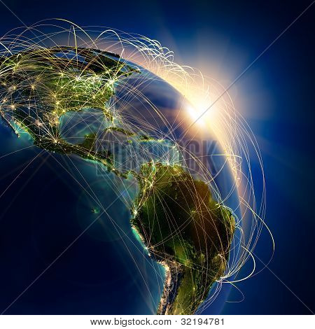 Picture or Photo of Highly detailed planet Earth at night lit by the rising sun with embossed continents illuminated by light of cities translucent and reflective ocean. Earth is surrounded by a luminous network representing the major air routes based on real data