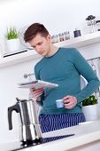 stock photo of newspaper  - young man drinking an espresso and reading the newspaper in the kitchen - JPG 