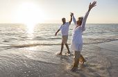 stock photo of man  - Happy senior man and woman couple dancing and holding hands on a deserted tropical beach at sunrise or sunset - JPG 