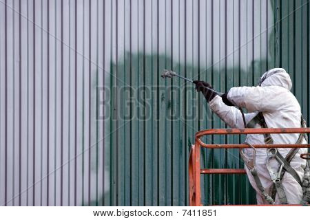 Picture or Photo of A commercial painter on an industrial lift spray painting a steel exterior wall or duct.