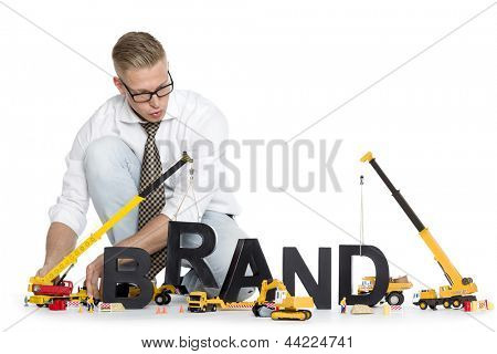 Picture or Photo of Build up a brand concept: Focused businessman building the word brand along with construction machines, isolated on white background.