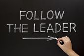 stock photo of hand  - Hand showing Follow The Leader written with white chalk on a blackboard - JPG 