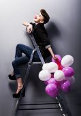 image of laughing  - Pretty cheerful fashion retro model teen girl laughing on ladder in studio with balloons - JPG 