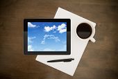 picture of computer  - Digital tablet with clouds on screen lying on worktable with paper pen and cup of coffee - JPG 