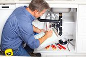 picture of workforce  - Young smiling plumber repairing sink in kitchen - JPG 