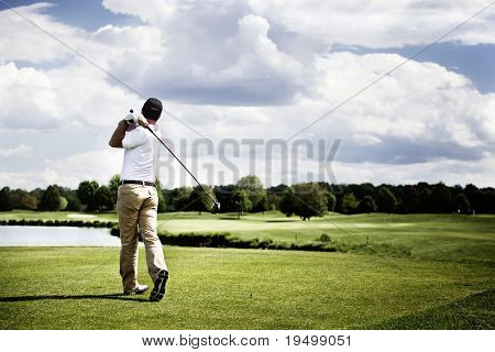 Picture or Photo of Male golf player teeing off golf ball from tee box, wonderful cloud formation in background.