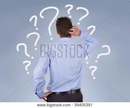 Picture or Photo of Confused businessman standing in front of a wall of question marks