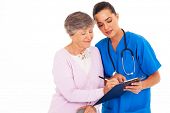 image of medical doctors  - senior woman signing medical form with help from nurse - JPG 