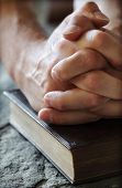 foto of religion  - Hands folded in prayer over a Holy Bible resting on a stone baptismal font - JPG 
