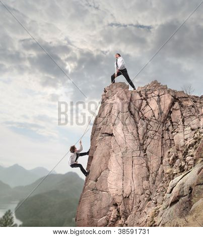 Picture or Photo of Businessman on the top of a rock helping an other businessman to climb it