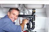 foto of workforce  - Young plumber fixing a sink at kitchen - JPG 