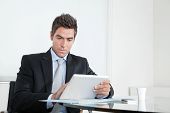 picture of businessmen  - Handsome young businessman at desk with digital tablet and coffee cup in office - JPG 