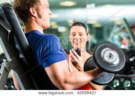Picture or Photo of Man or Bodybuilder with his personal fitness trainer in the gym exercising sport with dumbbells, closeup