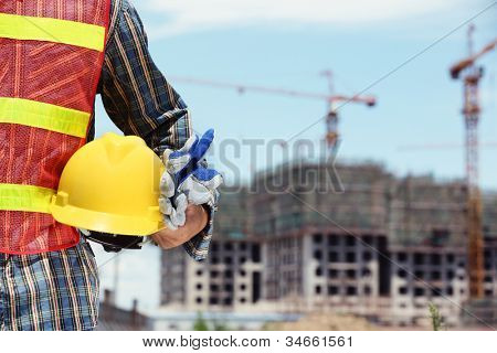 Picture or Photo of Man holding yellow helmet in front of construction site