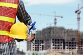 picture of health  - man holding yellow helmet in front of construction site - JPG 