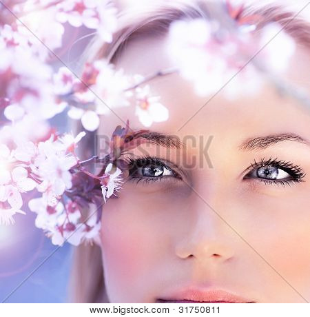 Picture or Photo of Sensual portrait of a spring woman, beautiful face, close up on blue eyes, female enjoying cherry blossom, dreamy girl with pink fresh flowers outdoor, seasonal nature, tree branch and natural beauty