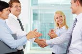 foto of handshake  - Successful businessmen handshaking while two females applauding after signing new contract - JPG 