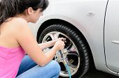 stock photo of pressure  - Young woman checking pressure and inflating car tires - JPG 