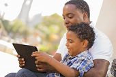 stock photo of american  - Happy African American Father and Mixed Race Son Having Fun Using Touch Pad Computer Tablet Outside - JPG 