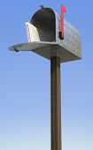 stock photo of blue sky  - a standard galvanized mailbox on post with mail and flag up over the blue sky - JPG 