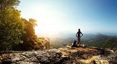 stock photo of standing  - Hiker with backpack standing on top of a mountain and enjoying stunning valley view - JPG 