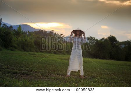Blonde Girl In Vietnamese Dress Lifts Hat Above Head On Field