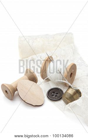 thread for sewing on wooden spools with needle, empty spool of thread, buttons, metal thimble, and a