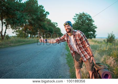 Young smilimg caucasian tourist hitchhiking along a road.