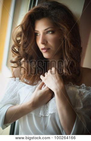 Attractive sexy brunette in white blouse posing provocatively in window frame