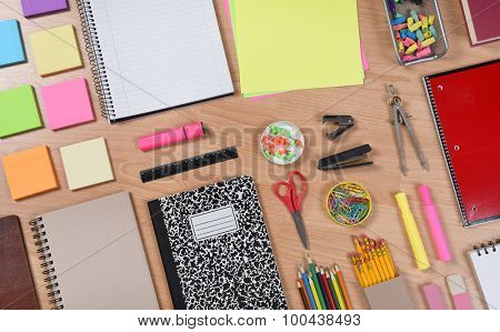 High angle shot of school supplies laid out on a wood desk. Back to School concept with paper, pads, pencils, notebooks, scissors, erasers and more. Horizontal format at an angle.