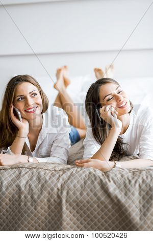 Two Beautiful Girls Talking And Smiling While Lying On A Bed