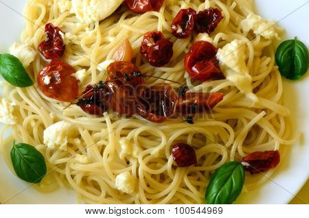 Spaghetti with mozzarella, dried tomatoes and basil on red background.