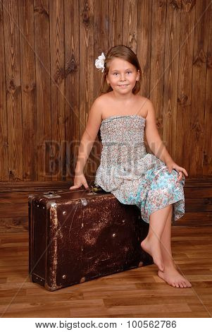 Smiling girl sits on the ancient brown scratched suitcase