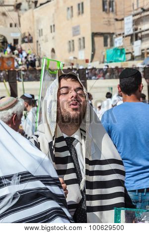 JERUSALEM, ISRAEL - OCTOBER 12, 2014: The area in front of Western Wall of  Temple filled with people.  Morning autumn Sukkot. The young guy in tallit prays
