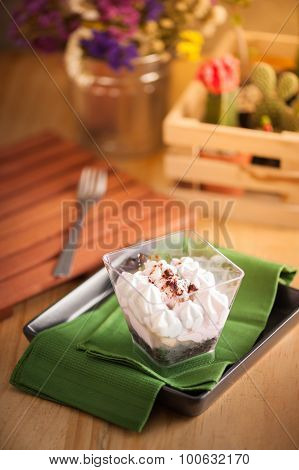 Banoffee pie in plastic cup on green napkin in black dish on wood table with afternoon scene