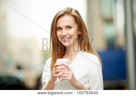 Young woman with coffe-to-go in street. Defocused background.