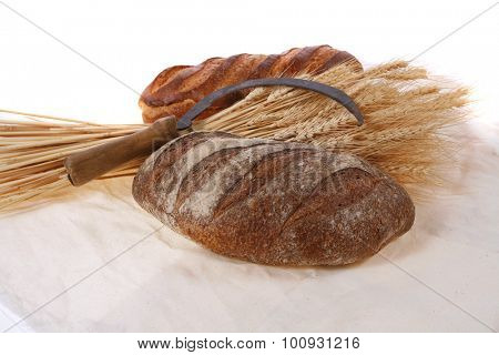 bunch of mown wheat ears with vintage handmade reaper hook sickle and rye and white dark french fresh bread loaf on light linen tablecloth