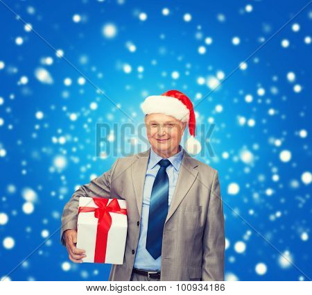business, christmas, xmas, happiness concept - smiling old man in suit and santa helper hat with gift