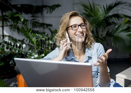 Beautiful young businesswoman using mobile phone while working at laptop.