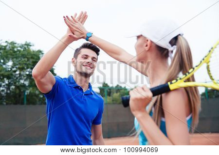 Male and female tennis players gives five at the tennis court after a match