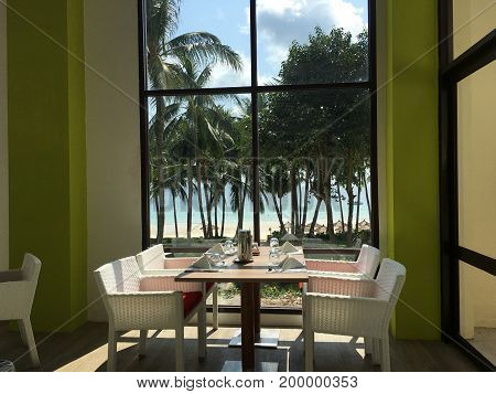 Set table and white chairs in front of a window with beach and sea view