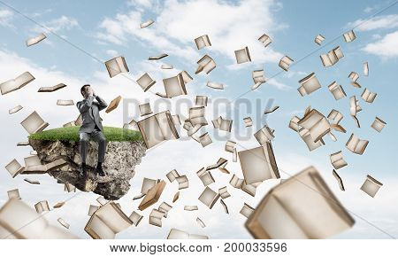 Young shocked businessman sitting on floating island and covering eyes with palms