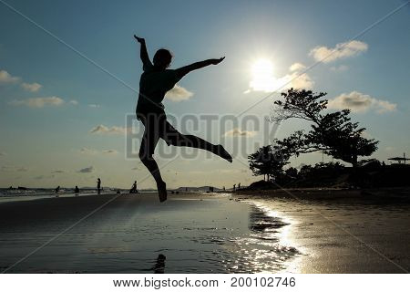 Silhouette woman jumping on the beach with sun and blue sky.