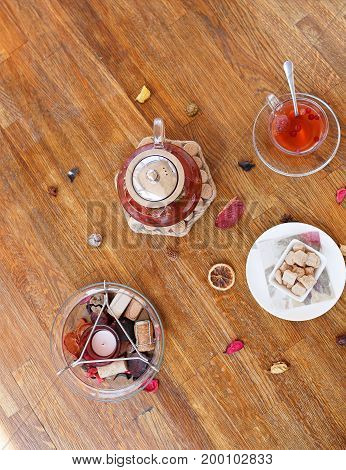 Top view of a composition of traditional breakfast. A plate of powdered cookies, chocolate sweets and biscuits on a wooden table background. A cup of red tea and strawberry spicy tea in a kettle.