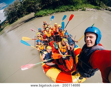 mountain Altai, RUSSIA - July 16, 2017: man in a helmet holds an action camera and makes selfie on the background of friends with oars, rafting