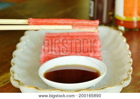 imitation crab stick made from fish dipping with soy sauce on chopsticks