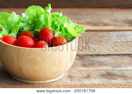 Fresh tomato and lettuce in wood bowl put on wood table. Side view of tomato and green oak lettuce with copy space for background. Fresh green oak lettuce and tomato prepare for cooking.