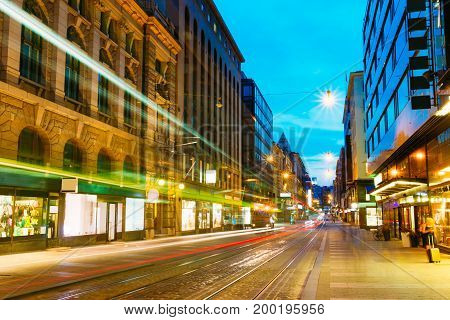 Helsinki, Finland. Tram Departs From A Stop On Street Aleksanterinkatu In Helsinki. Night View Of Aleksanterinkatu Street In Kluuvi District In Evening Or Night Illumination.